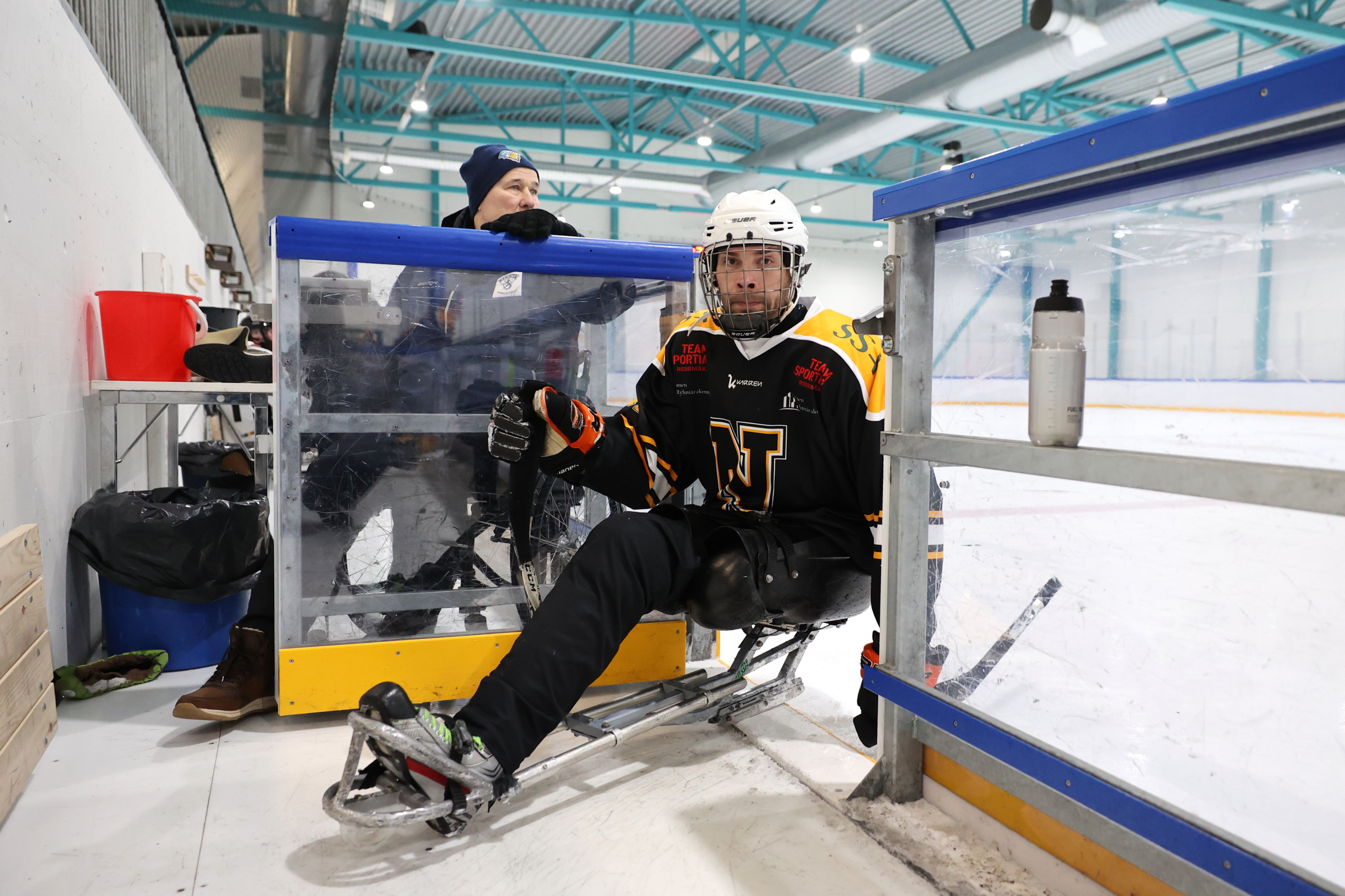 Parajääkiekkoilija liukumassa jäältä vaihtoaitioon jääkiekkokelkallaan.